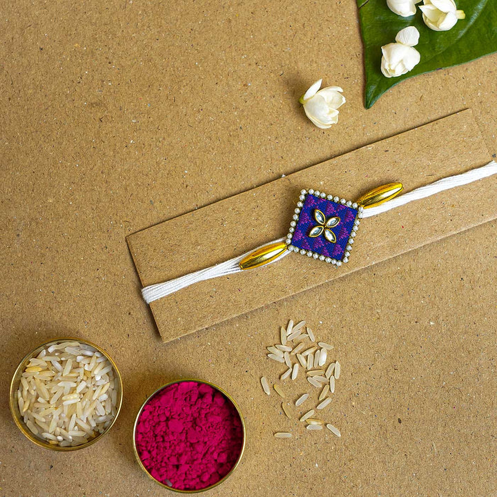 Handmade Purple Diamond Fabric And Mdf Rakhi With Roli Chawal - Flat Lay with Rice and Color Powder