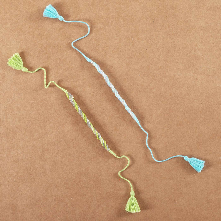 Handmade Beaded Zari Strings Rakhi With Roli Chawal Set Of 2 - Flat Lay on Brown Surface