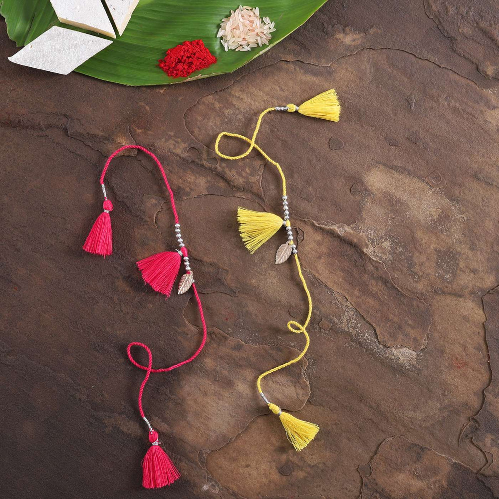 Handmade Yellow And Red Tassel Rakhi With Roli Chawal Set Of 2 - Flat Lay with Rice and Paper