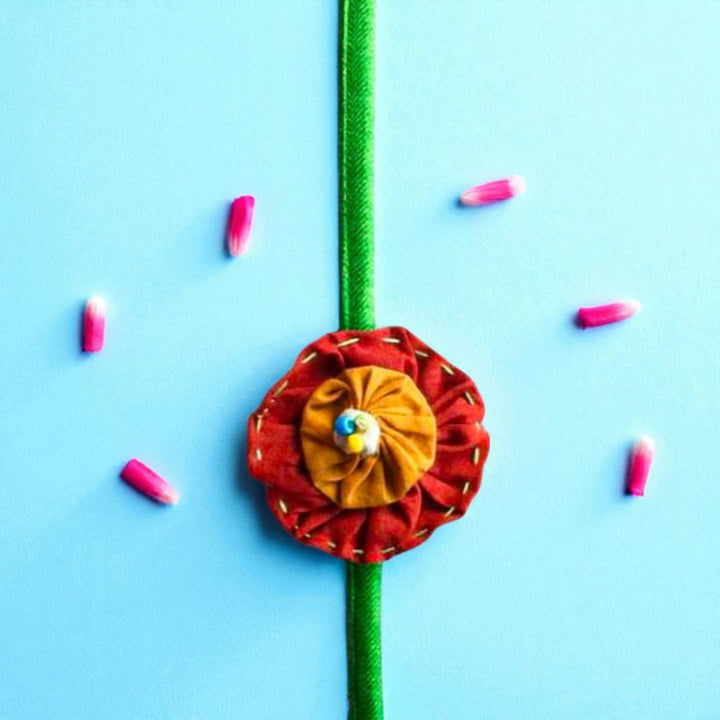 Handmade Brown And Orange Floral Upcycled Fabric Rakhi With Roli Chawal For Brother - Top View with Flower Decoration