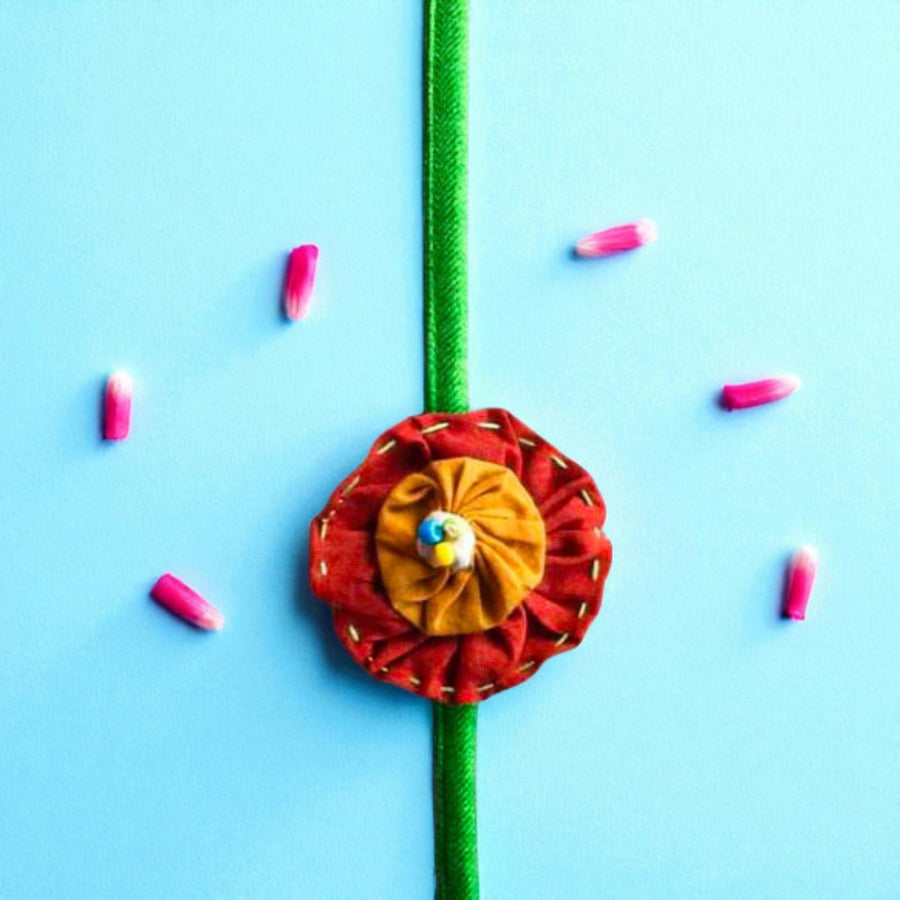 Handmade Brown And Orange Floral Upcycled Fabric Rakhi With Roli Chawal For Brother - Top View with Flower Decoration