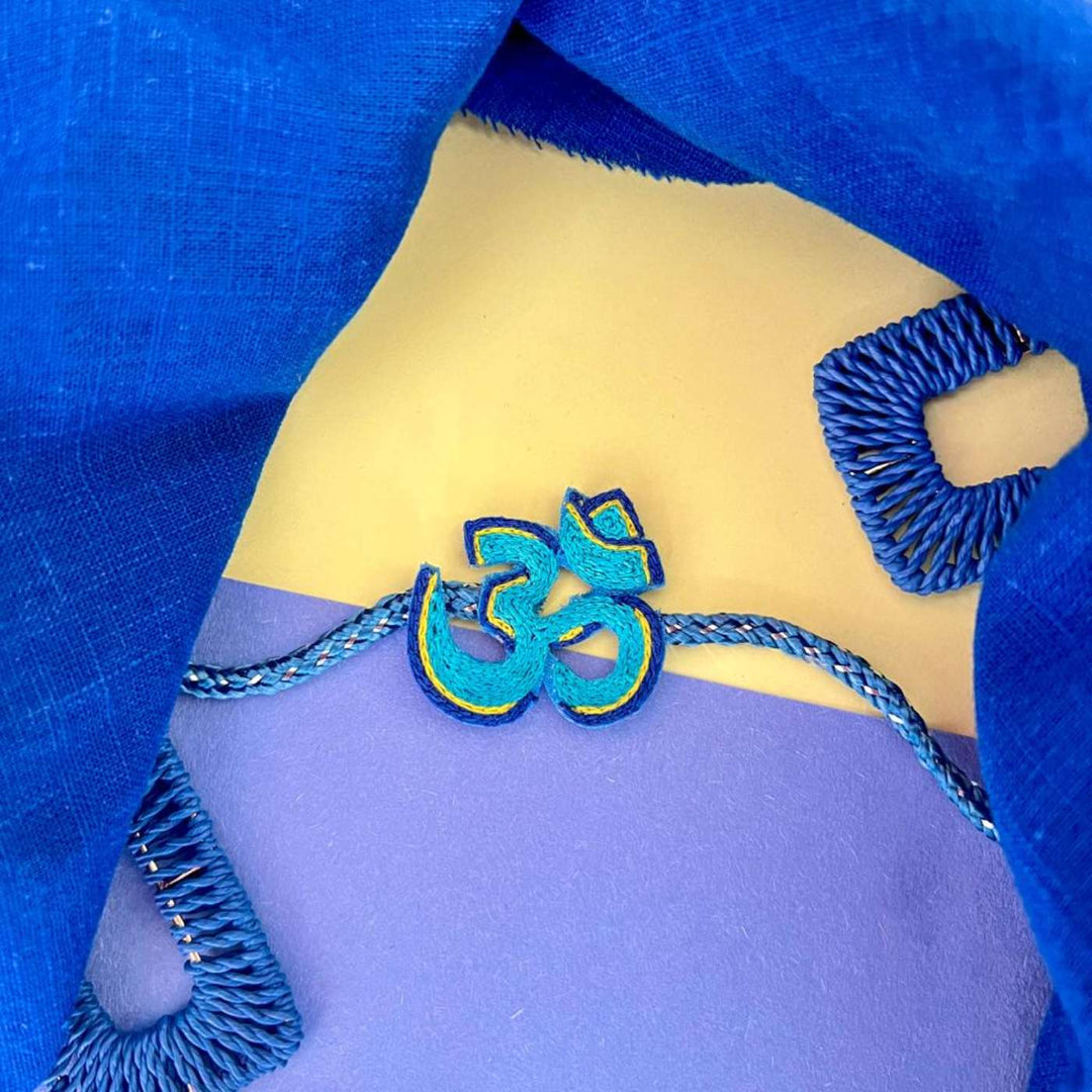 Handmade Beaded Om Rakhi With Roli Chawal - Styled with blue fabric background
