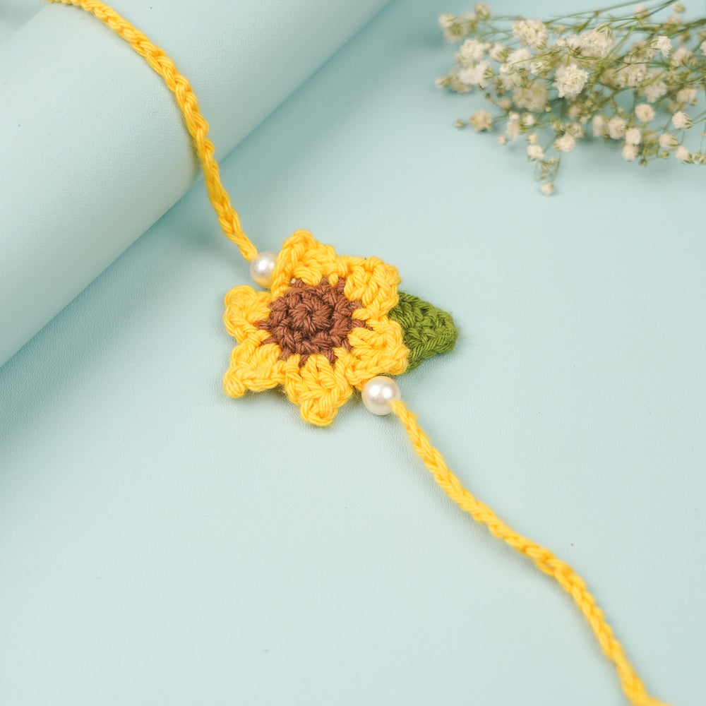 Handmade Crochet Sunflower Rakhi With Roli Chawal 2 - Top view angled on rolled surface