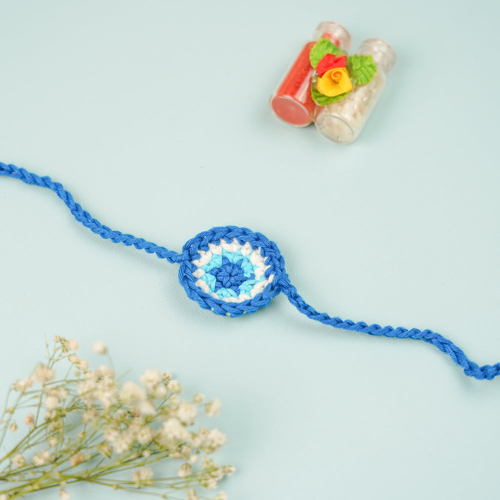 Handmade Crochet Evil Eye Rakhi With Roli Chawal - Flat lay with decoration items