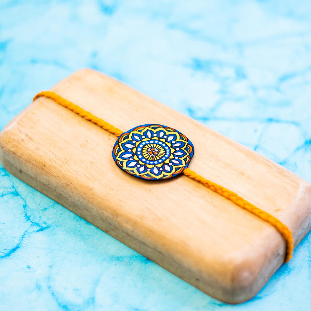 Hand Painted Seed Rakhi Orange - On Light Wooden Display Block