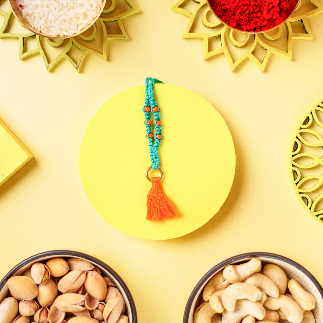 Teal Macrame Cotton Rakhi With Orange Beads Tassle - Flat lay of bracelet with yellow background