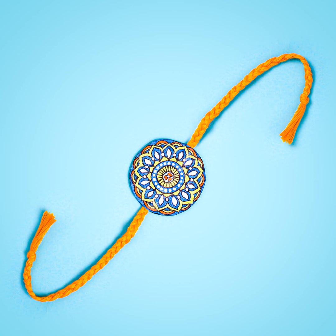 Hand Painted Seed Rakhi Orange - Flat Lay with Blue Background