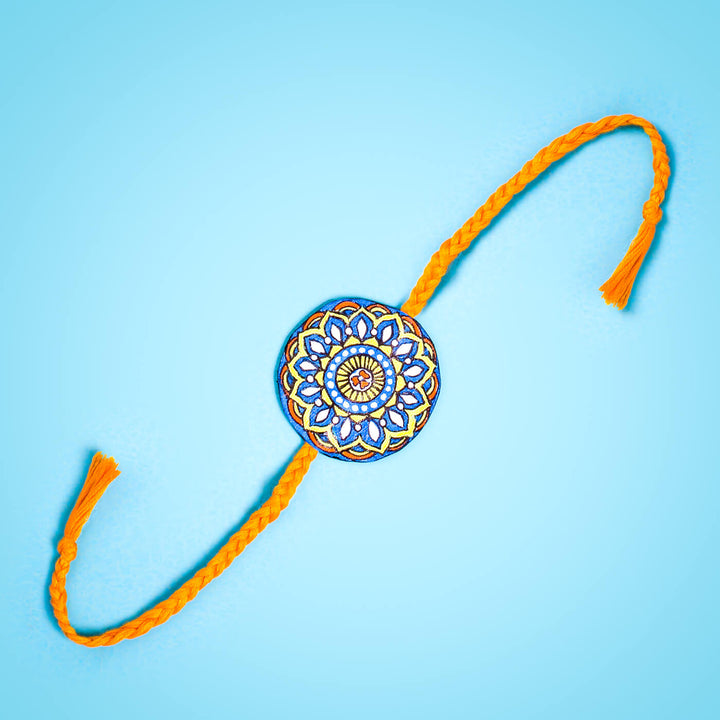 Hand Painted Seed Rakhi Orange - Flat Lay with Blue Background